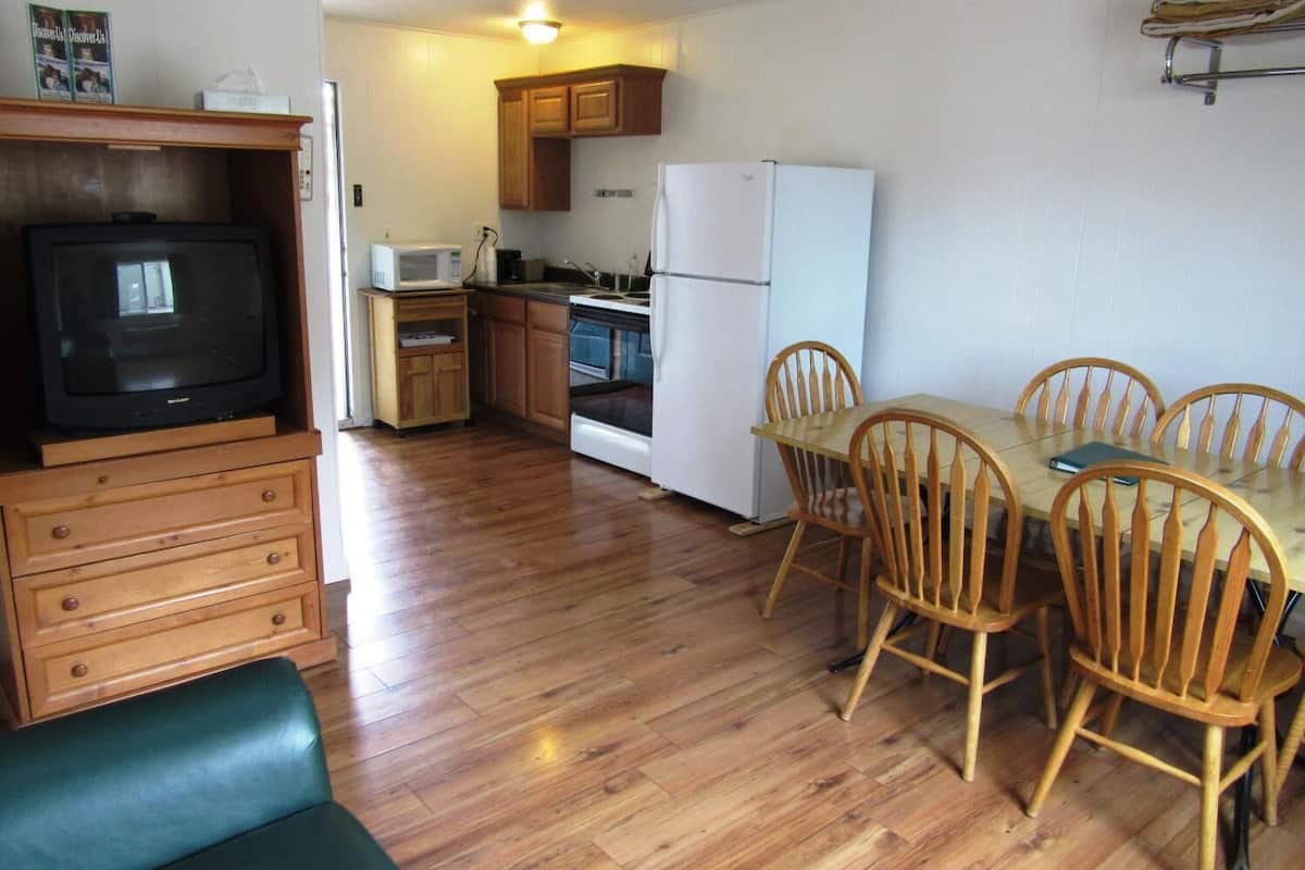 A compact kitchen with wooden cabinets, a refrigerator, a microwave, and a dining table with chairs.