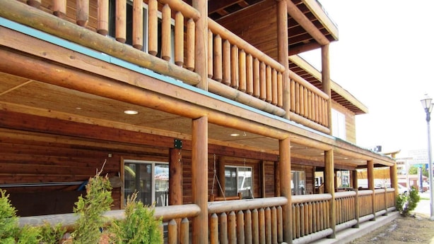 Un bâtiment en bois à deux étages, doté d’un balcon, de fenêtres et d’une zone pavée agrémentée de plantes.