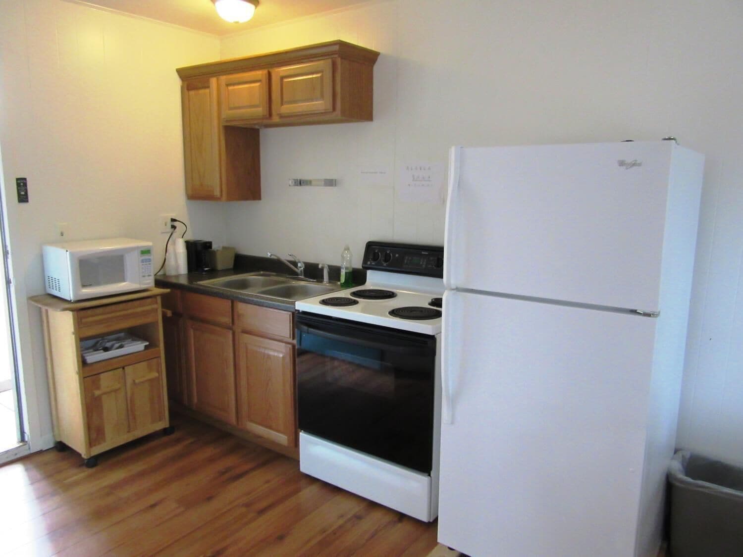 A compact kitchen with wooden cabinets, a white microwave, a stove, and a refrigerator.