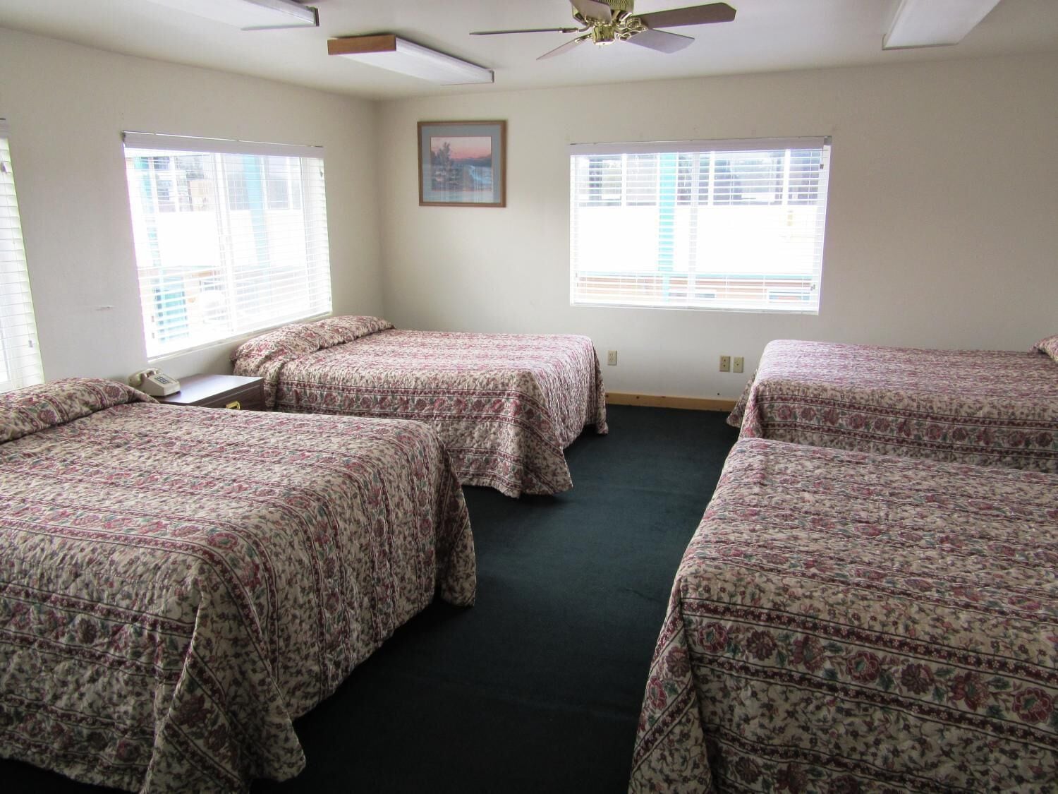 Une chambre avec trois lits, chacun agrémenté de draps à motifs floraux, un ventilateur de plafond et deux fenêtres équipées de stores.