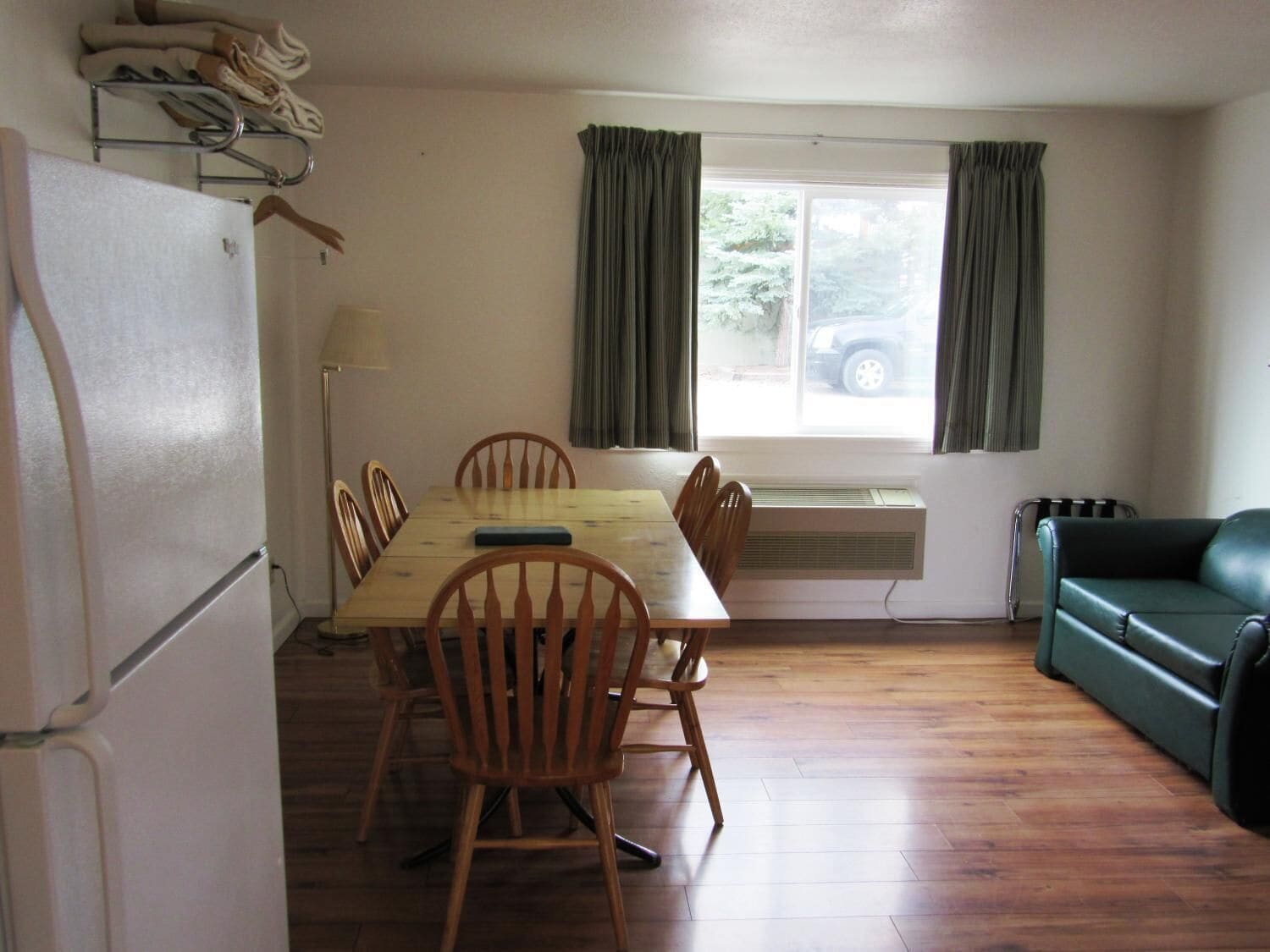 A compact kitchen with a dining table, chairs, a refrigerator, an air conditioner, and a green sofa.