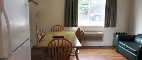 A compact kitchen with a dining table, chairs, a refrigerator, an air conditioner, and a green sofa.