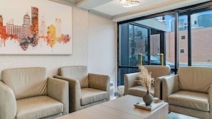 A modern hotel lobby with leather armchairs, a wooden coffee table, and a cityscape painting.