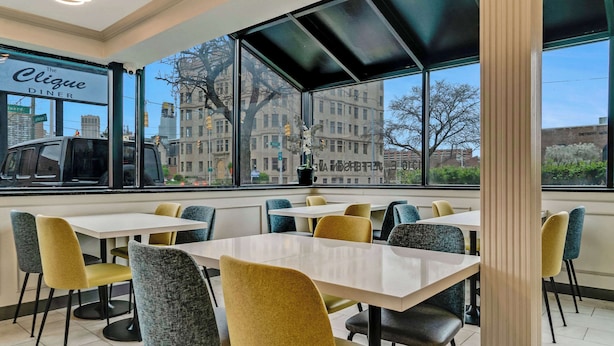 A dining area with tables and chairs, large windows with a city view, and a sign reading "The Clique Diner".