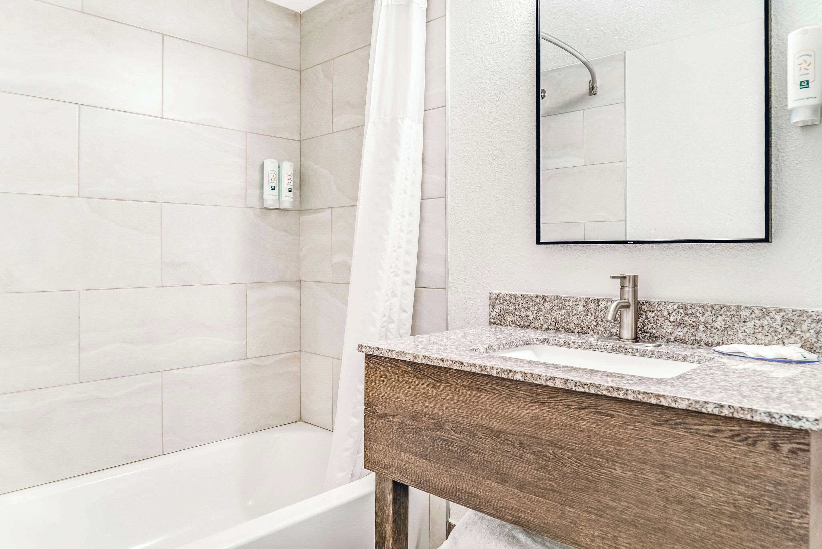 A modern bathroom with a shower, a sink with a granite countertop, and a mirror.