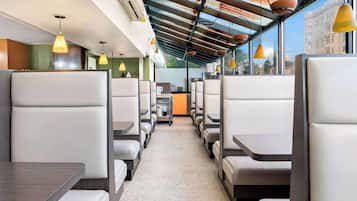 Un interior de restaurante moderno con asientos tipo cabina, iluminación colgante y vistas de la ciudad a través de amplios ventanales.
