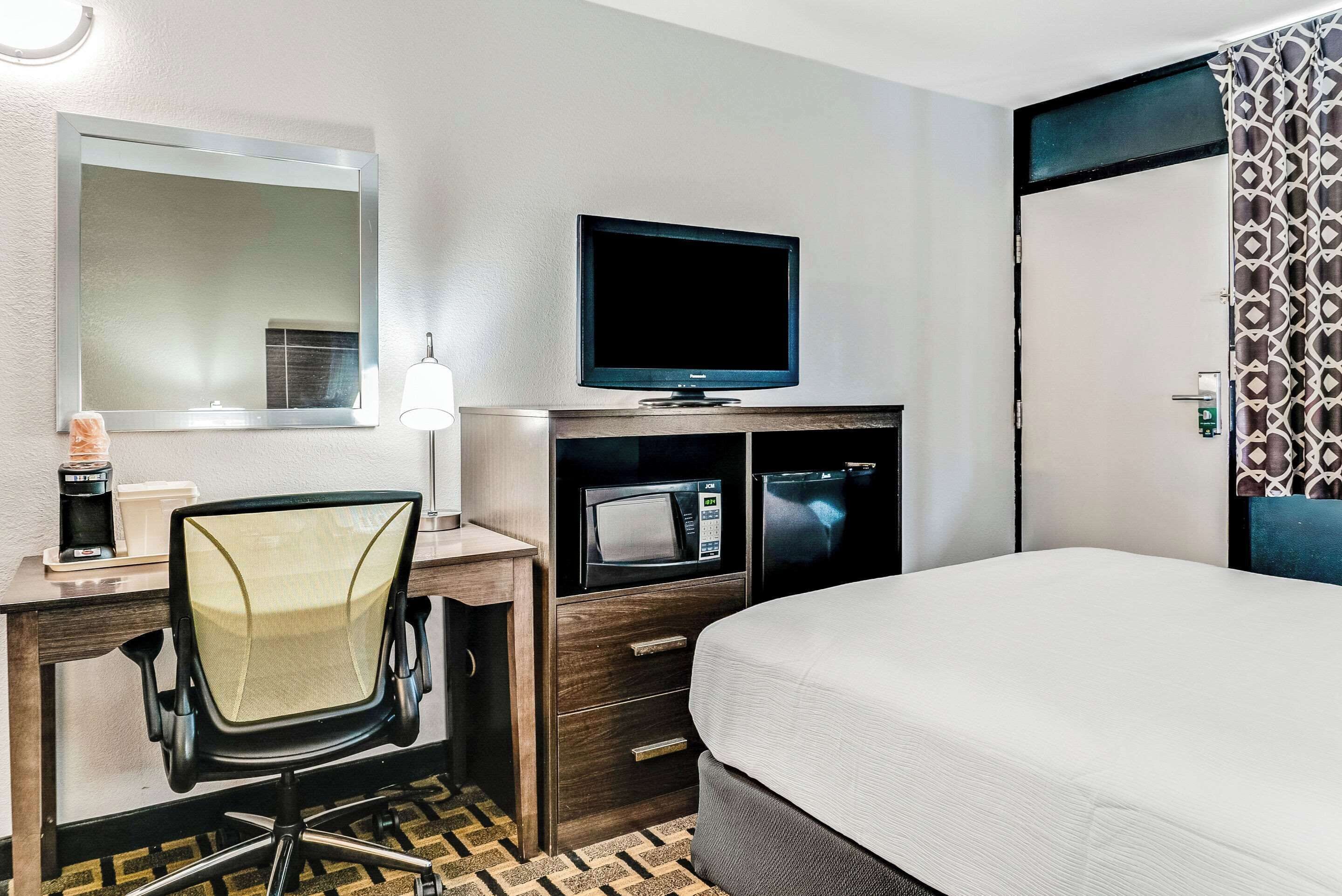 Une chambre d’hôtel comprenant un lit, un bureau avec une chaise, une télévision, un four à micro-ondes et un miroir.