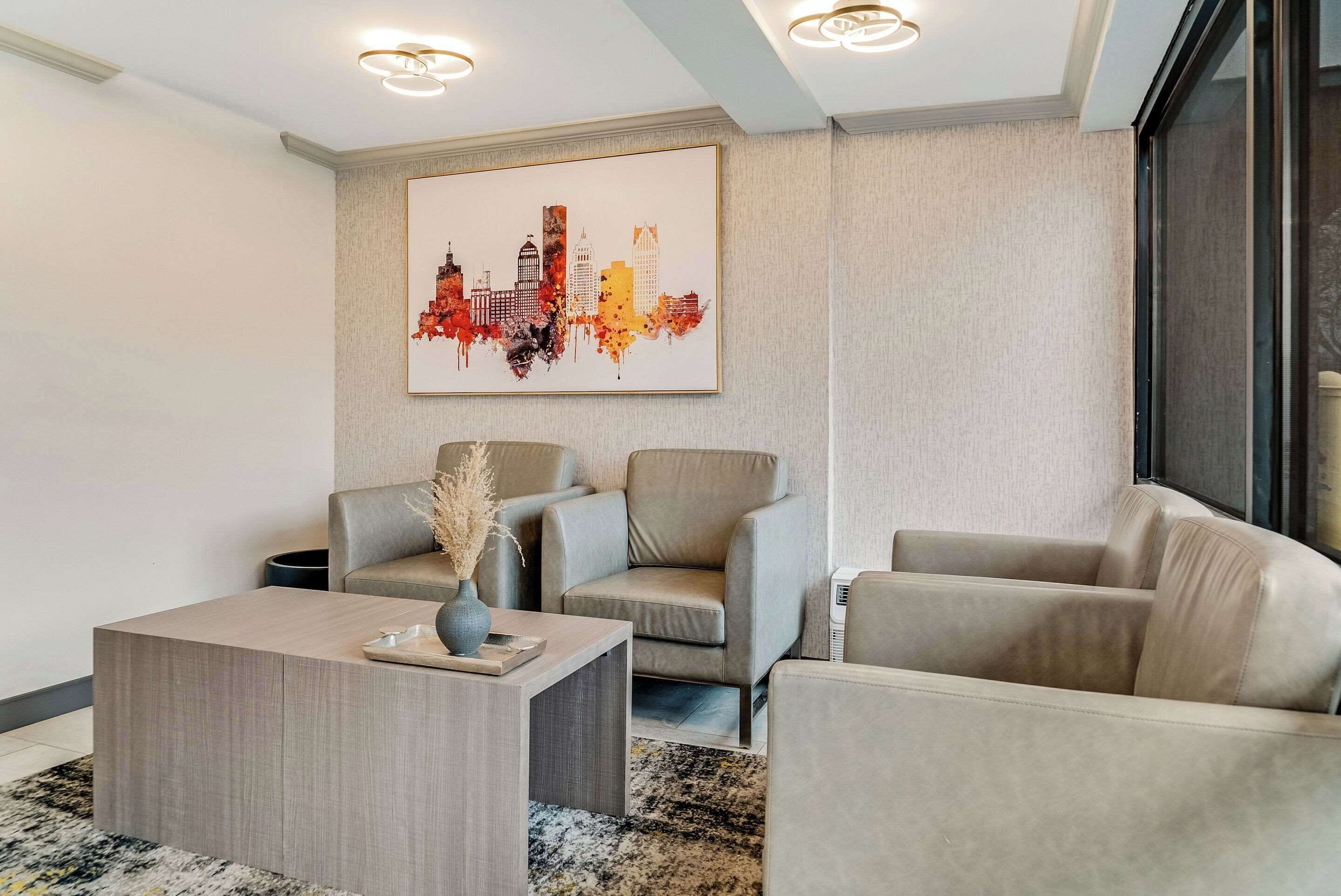 Una sala de estar moderna con una obra de arte del horizonte de la ciudad, dos sofás, una mesa de centro y un jarrón con plantas secas.