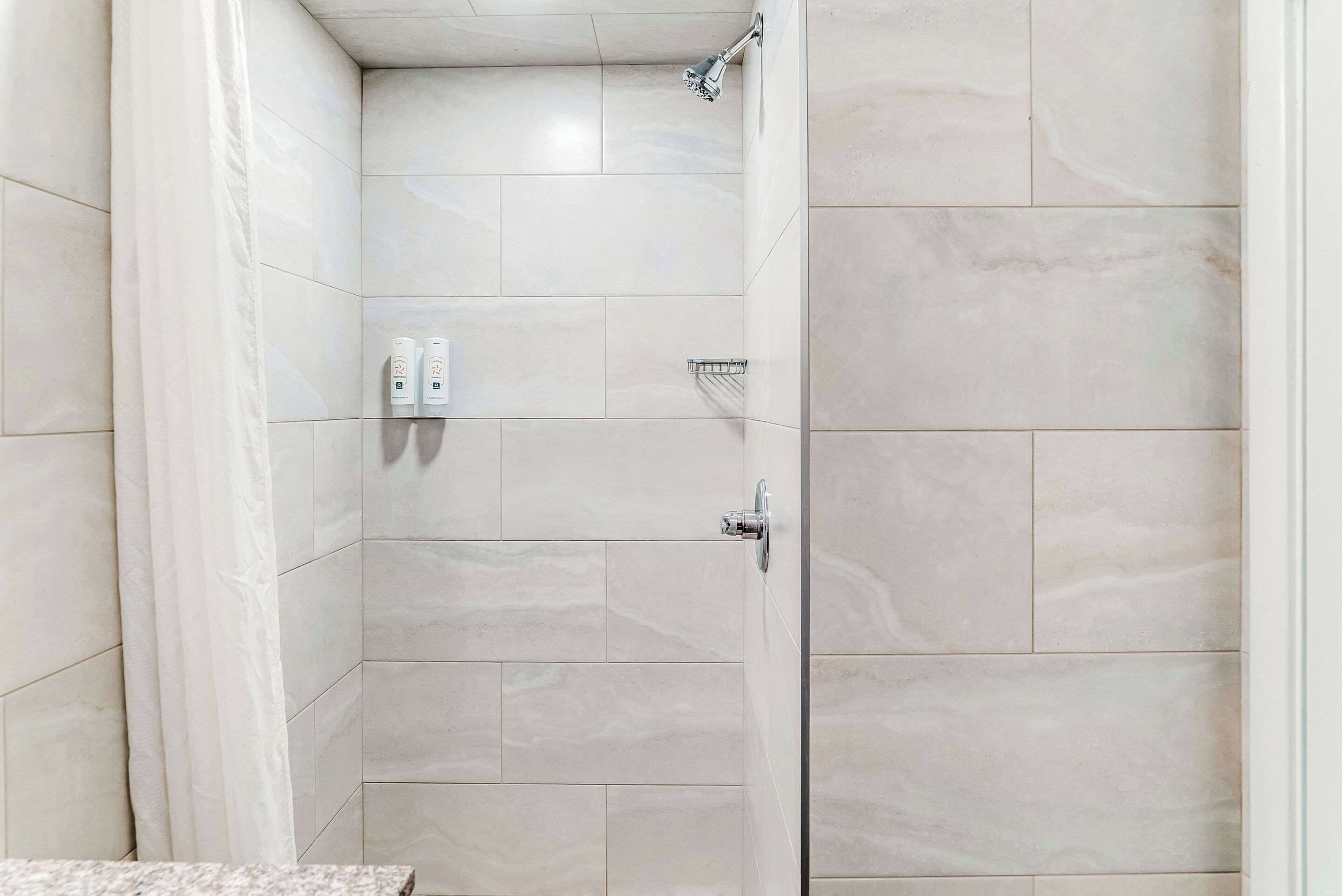 A shower with a tiled wall, a showerhead, and a control panel.