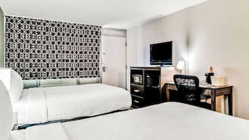 Una habitación de hotel con dos camas, un escritorio con televisor y un papel tapiz estampado.