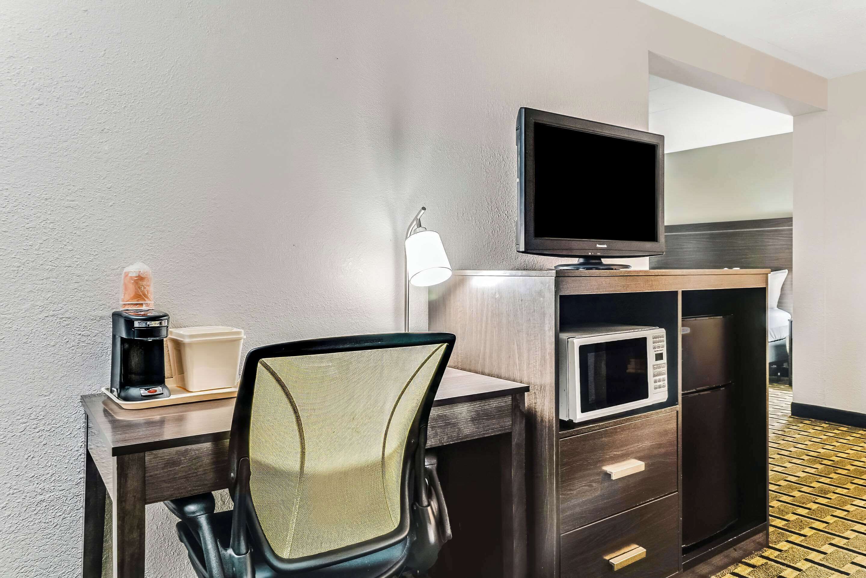 A hotel room with a desk, a chair, a television, a microwave, and a refrigerator.