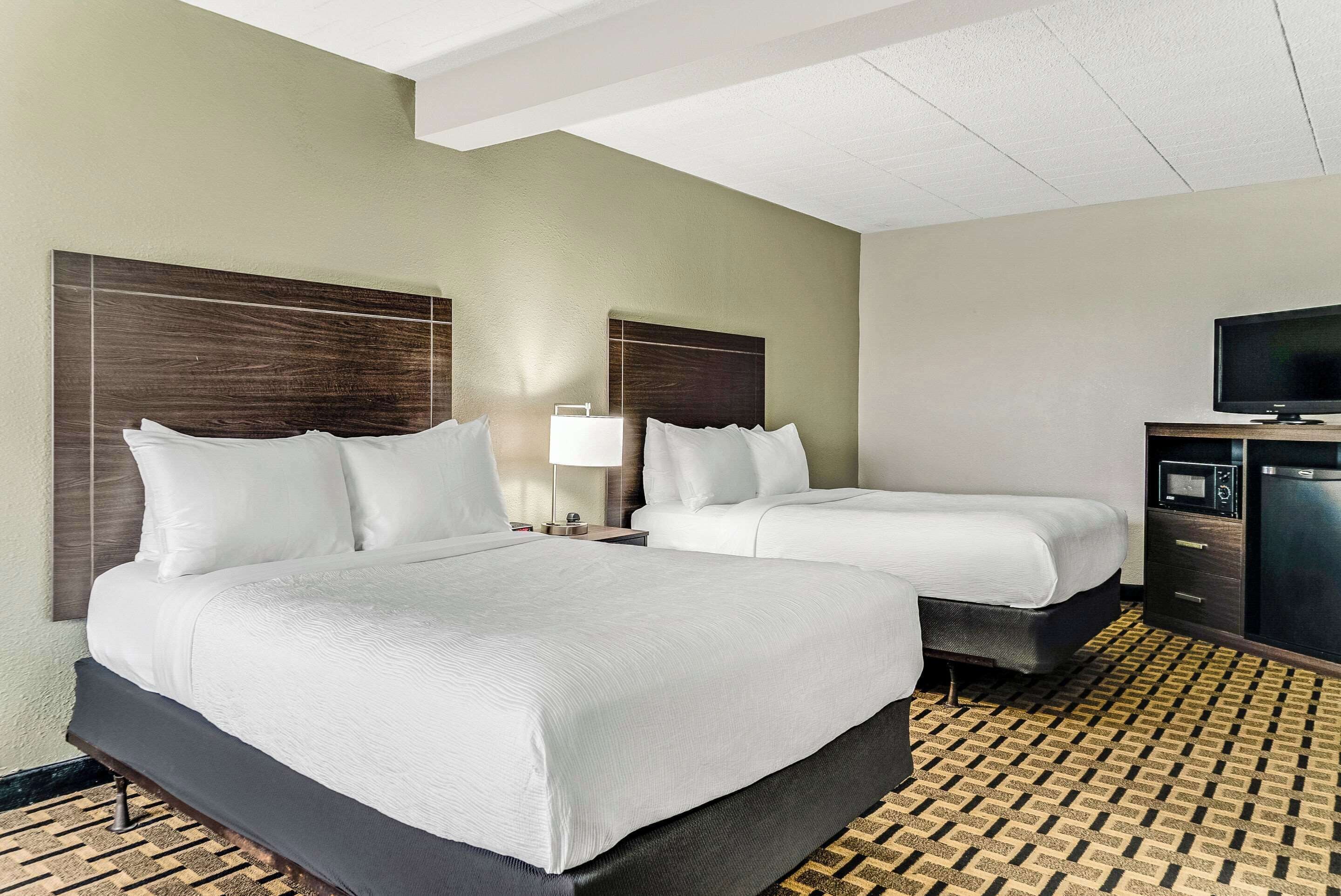 A hotel room with two beds, a TV, a desk, and a patterned floor.