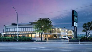 A modern hotel with a glass facade, a well-lit entrance, and a parking area visible.