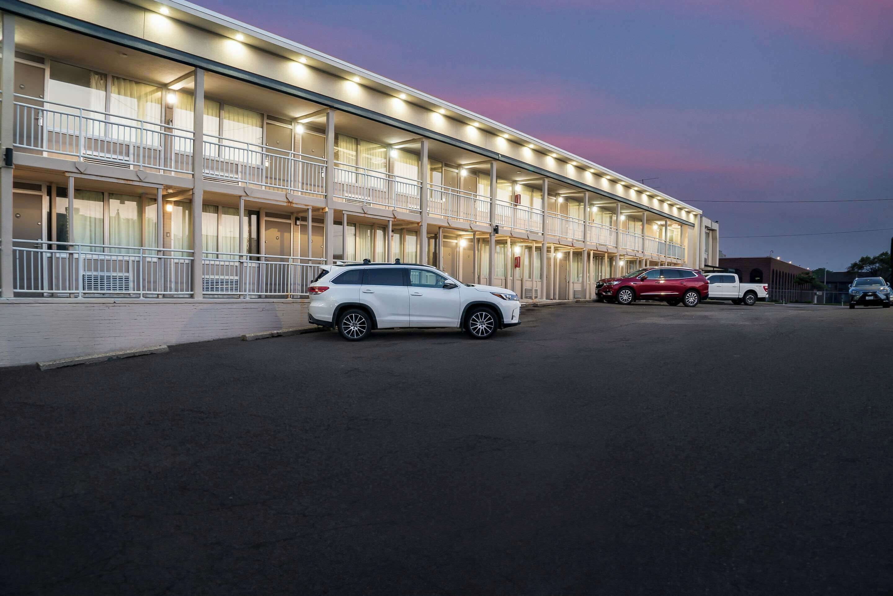 Un motel de varios pisos, con balcones y un estacionamiento con varios automóviles.