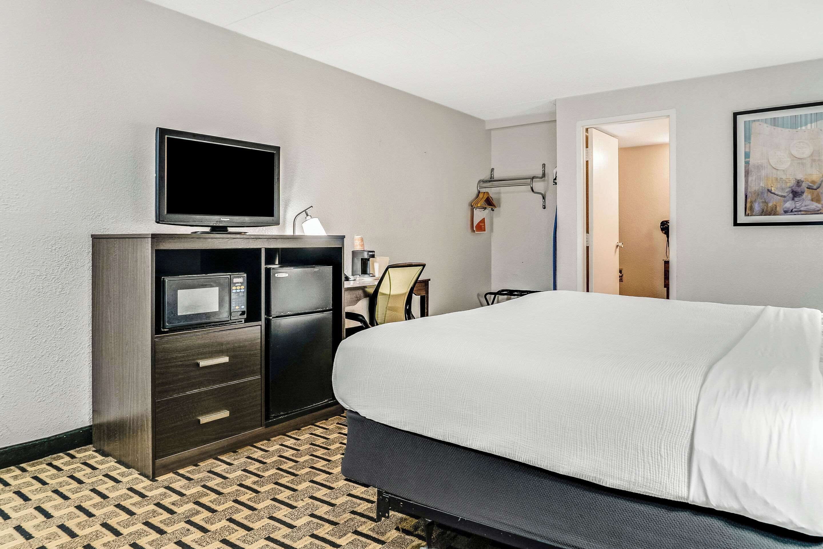 A hotel room with a bed, a TV, a minibar, a desk, and a chair.