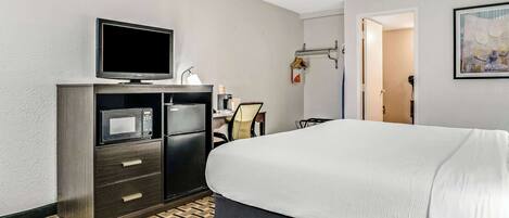 A hotel room with a bed, a TV, a minibar, a desk, and a chair.