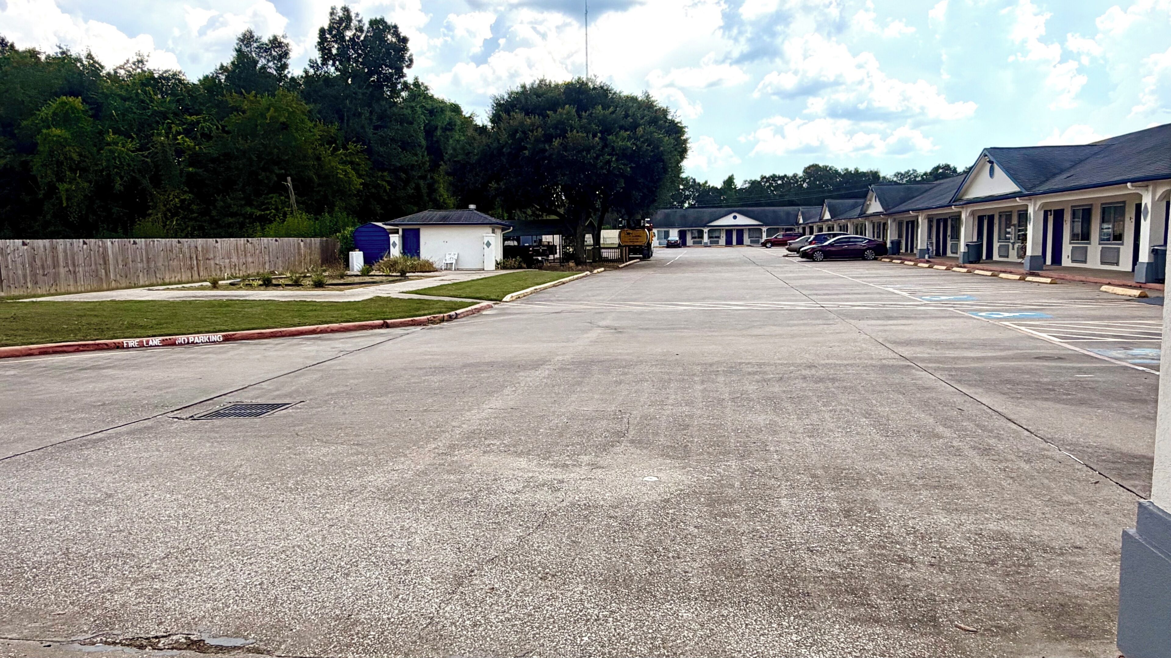 A parking lot with a fire lane, a small building, and a row of hotel rooms.