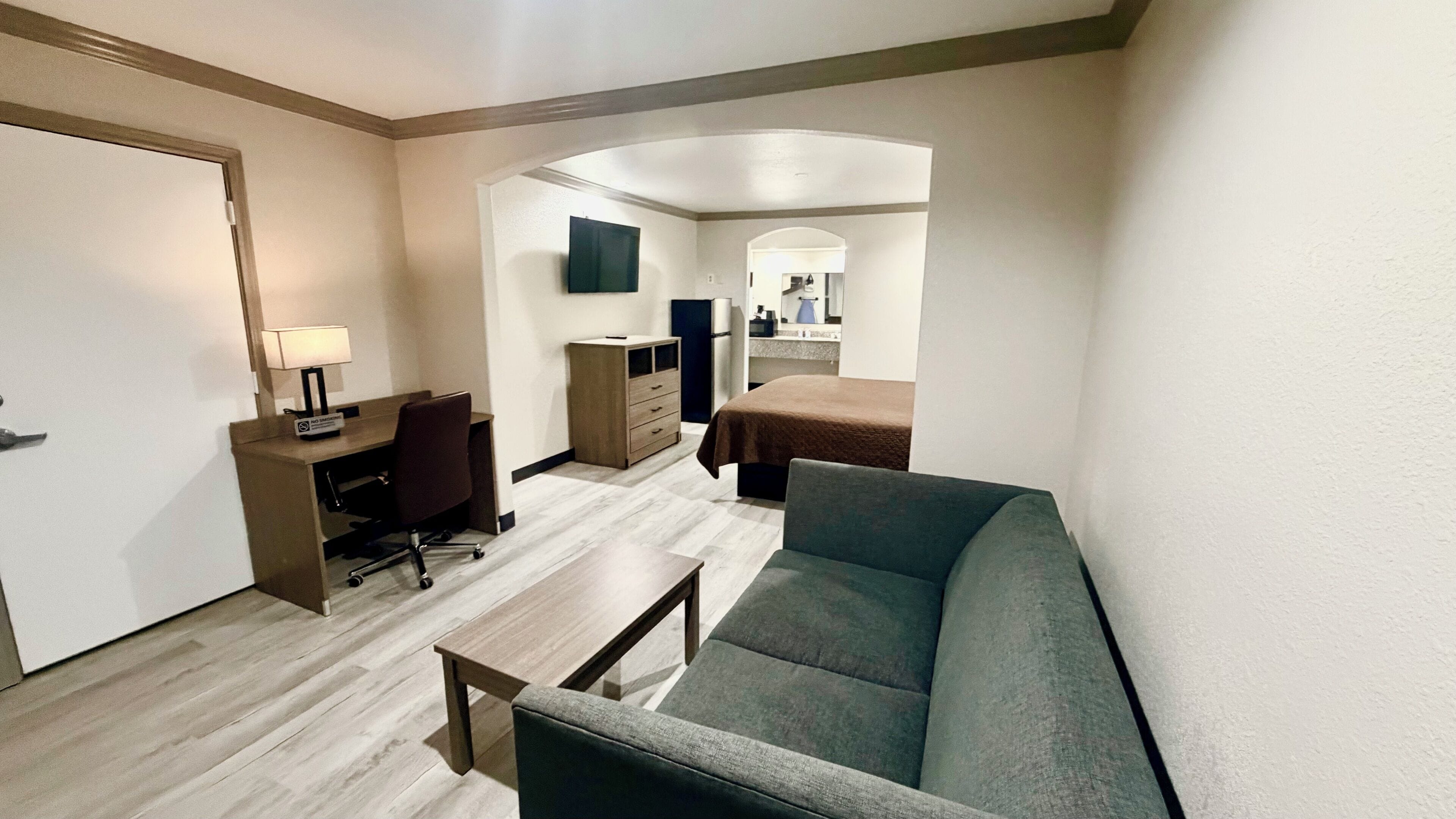 A hotel room with a sofa, a desk with a chair, a small table, a dresser, and a bed.