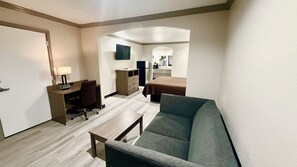 A hotel room with a sofa, a desk with a chair, a small table, a dresser, and a bed. - Luxury Inn & Suites Liberty (Liberty)