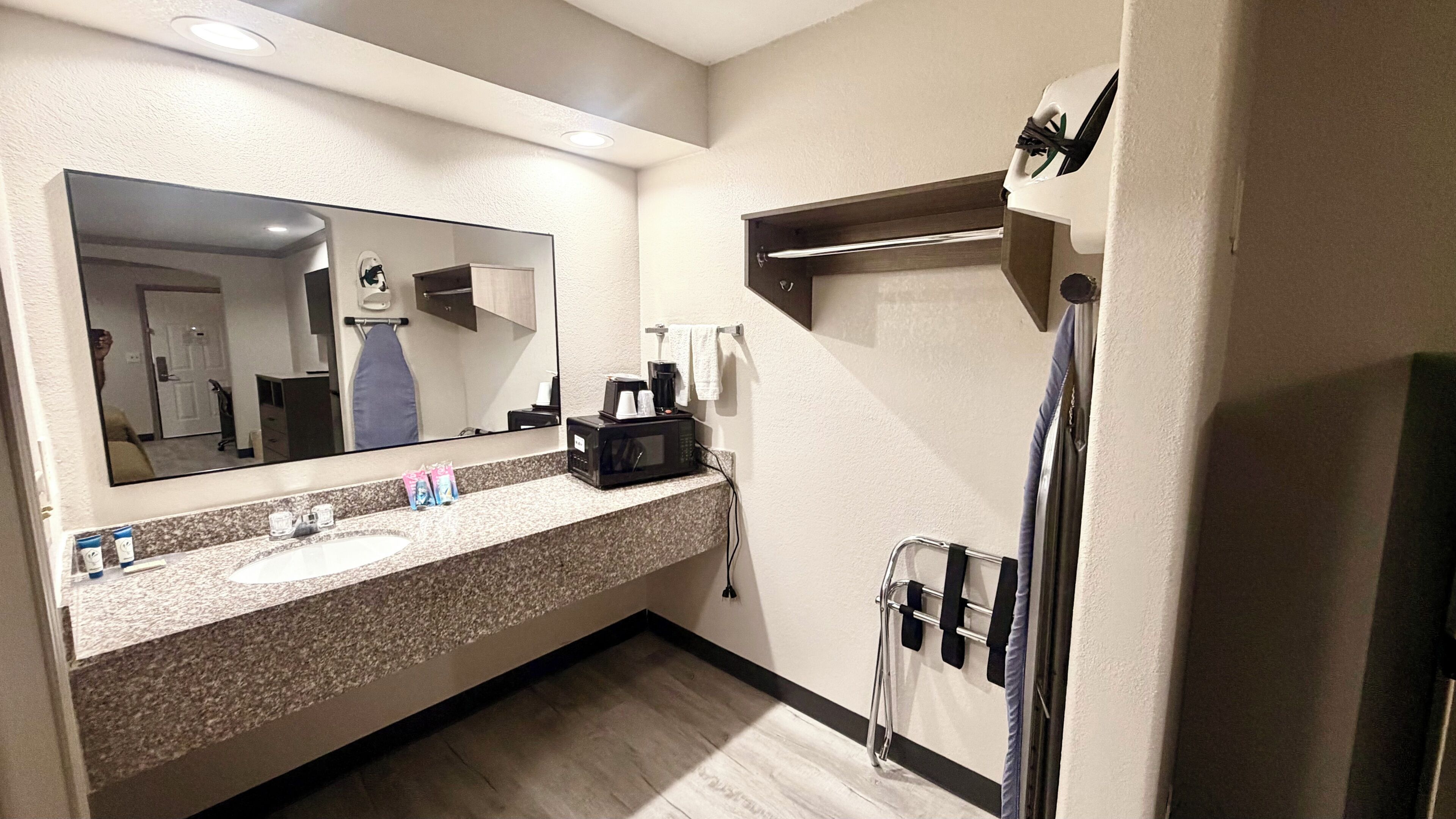 A hotel bathroom with a sink, mirror, towel rack, and a shower area.