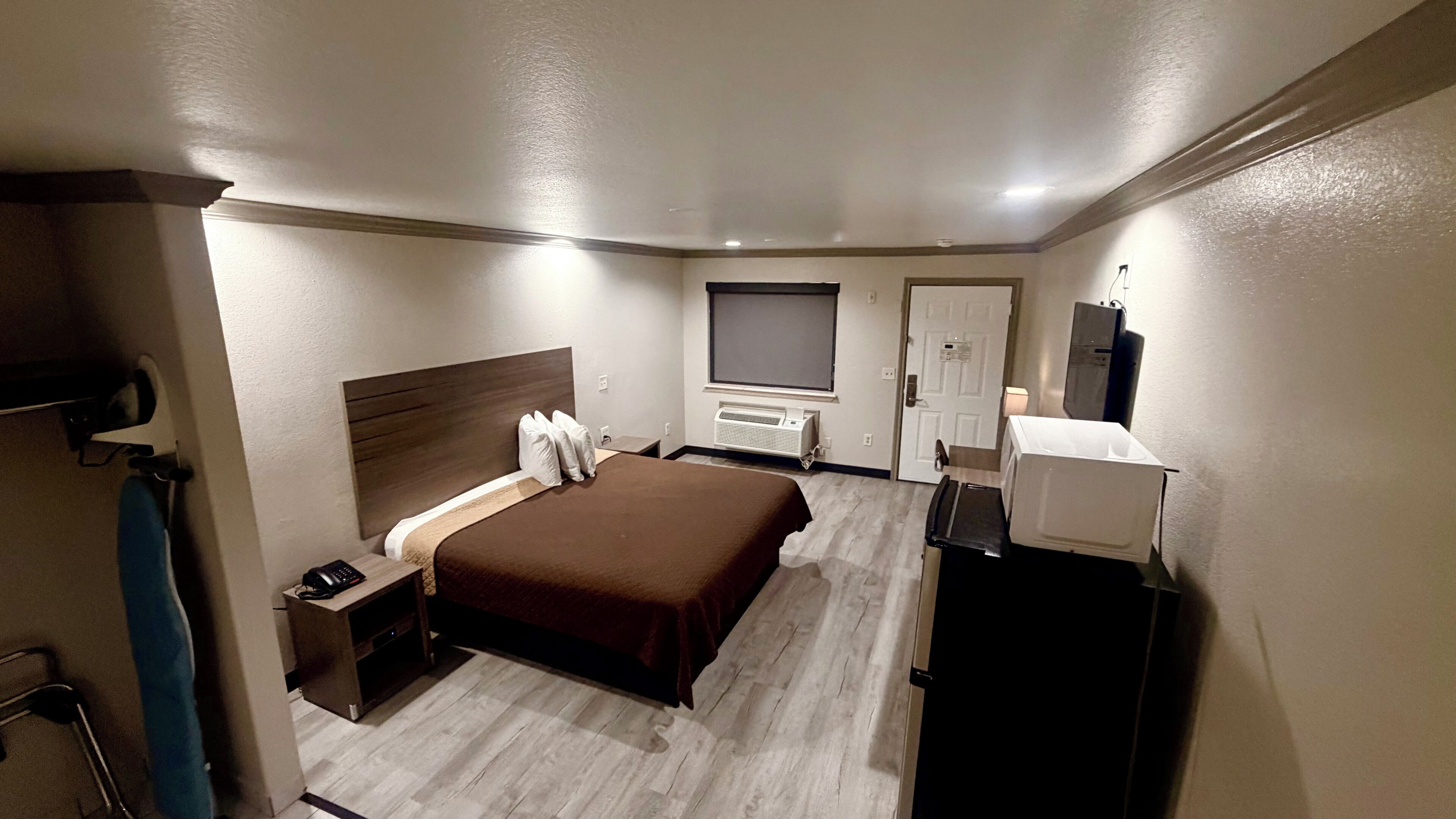 A hotel room with a bed, bedside table, a desk with a chair, a wardrobe, a mirror, and a television.