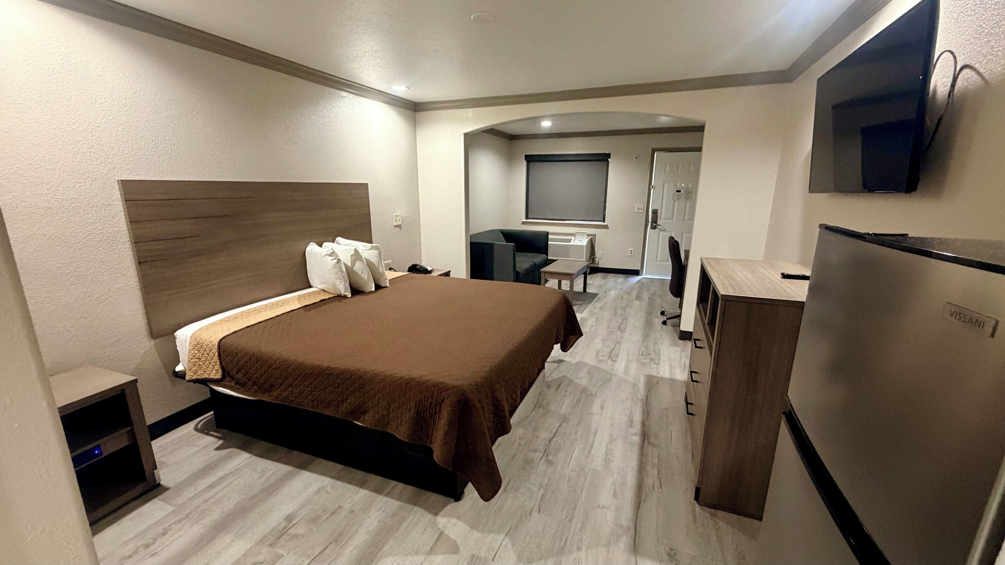 A hotel room with a bed, a desk, a chair, a television, and a refrigerator.