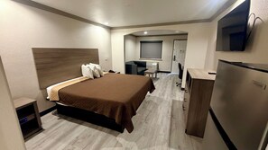 A hotel room with a bed, a desk, a chair, a television, and a refrigerator. - Luxury Inn & Suites Liberty (Liberty)