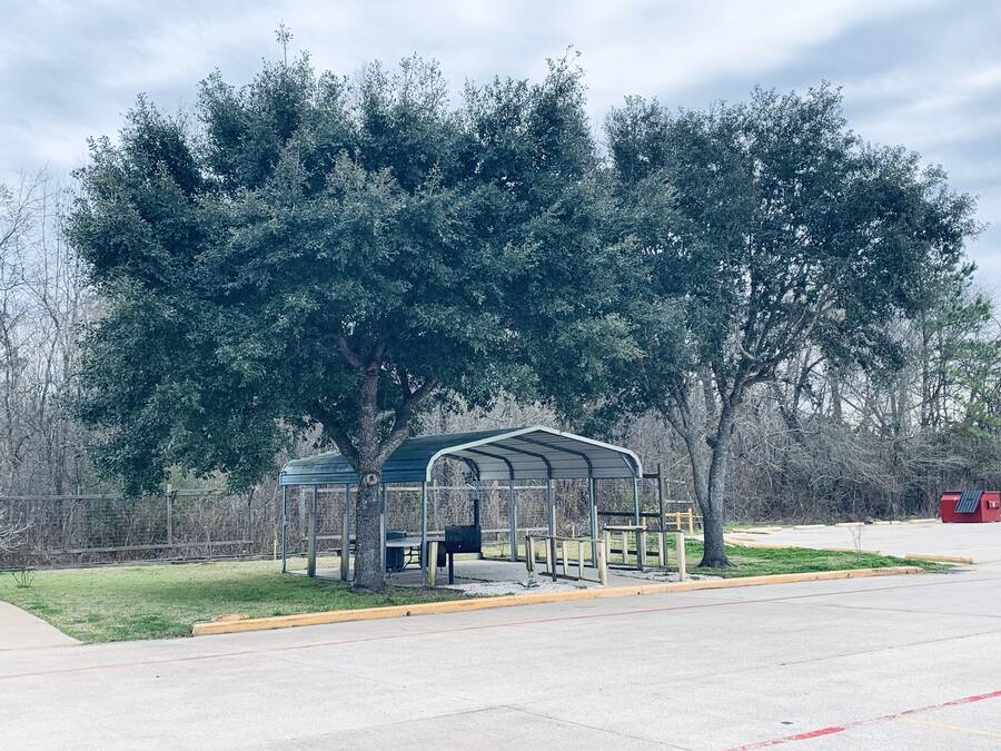 A covered picnic area with benches and a trash can, surrounded by trees.