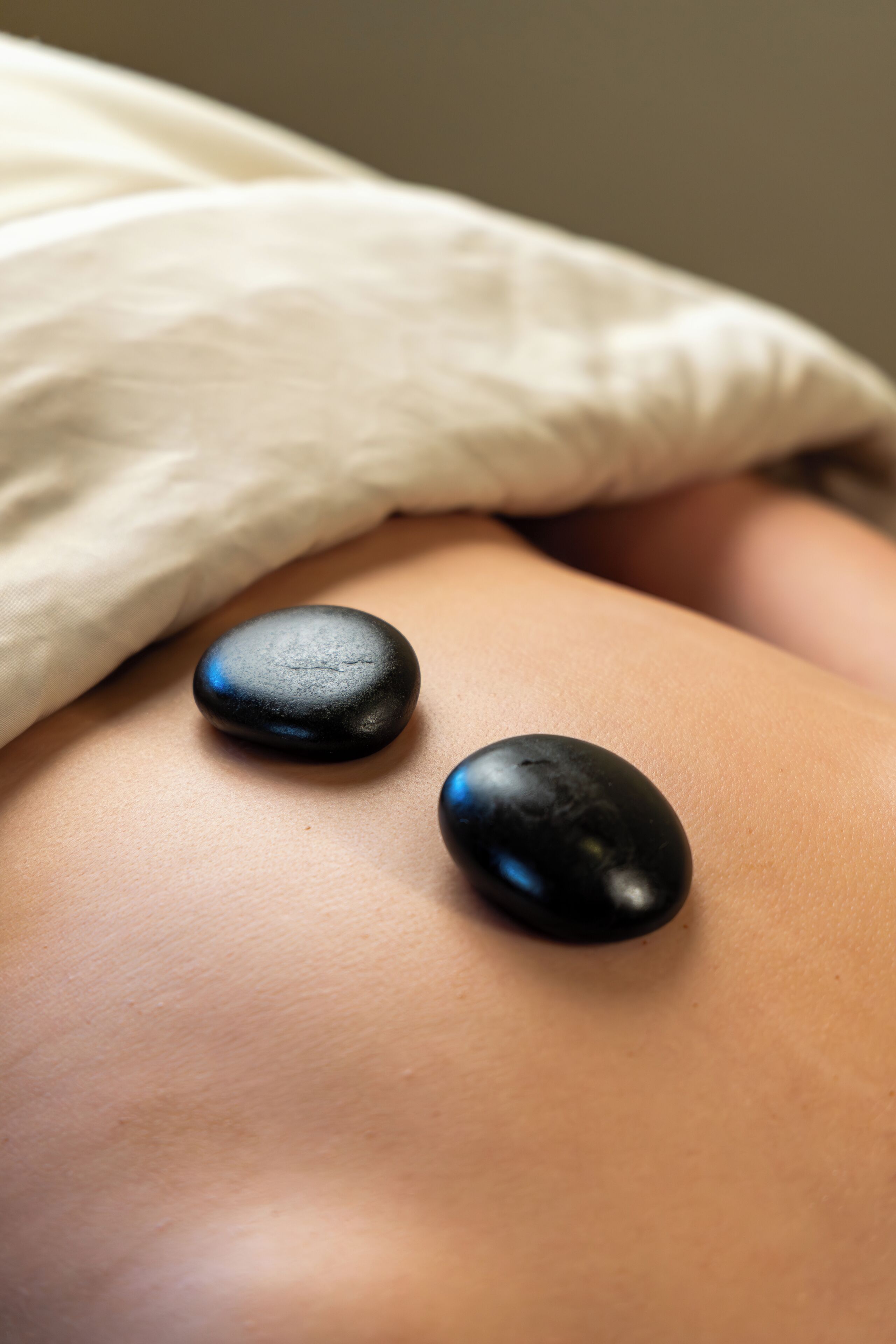 Nærbillede af en massage med to sorte sten på ryggen.