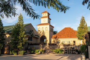 A building with a prominent tower, a large arched entrance, and a courtyard with barrels.