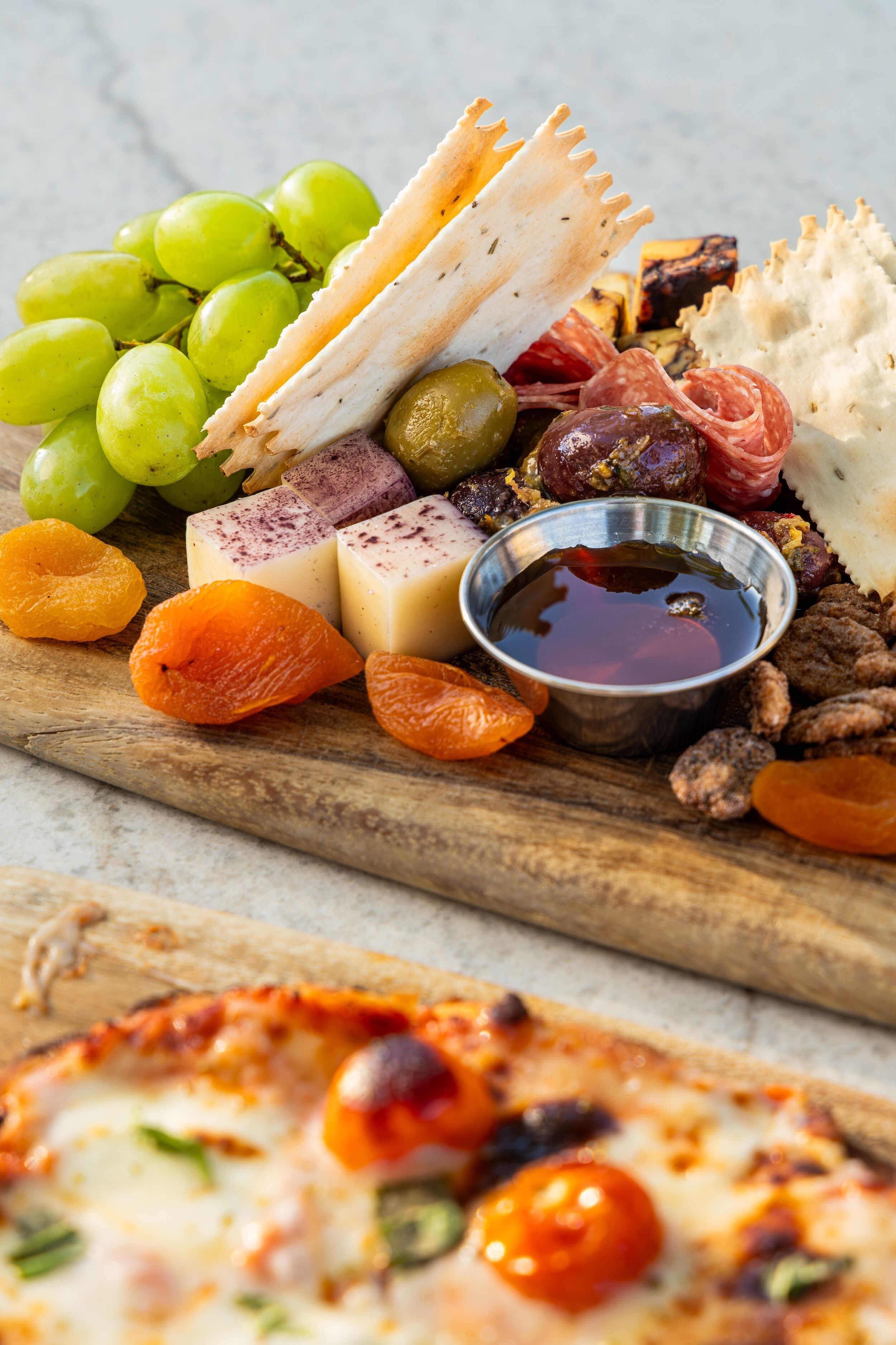 Une planche de charcuterie avec divers fromages, des fruits, des noix et un petit bol de sauce.