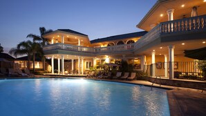 Ein großer Pool mit überdachter Terrasse, Palmen und einem zweistöckigen Gebäude mit Balkon.