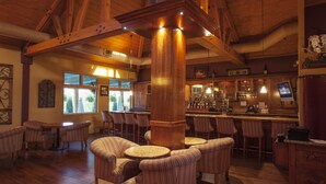 A spacious bar area with high wooden beams, multiple seating options including round tables and cushioned chairs, and a well-lit bar counter. - South Coast Winery Resort and Spa (Temecula)