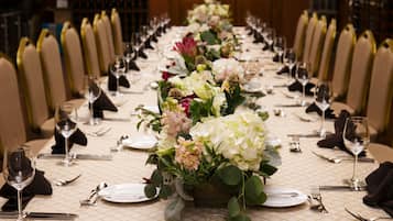 A long dining table with floral centerpieces, set with white plates, silverware, and wine glasses.