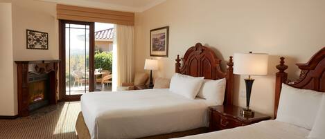 A hotel room with two beds, a fireplace, a dining area with a table and chairs, and a view of the outdoors.