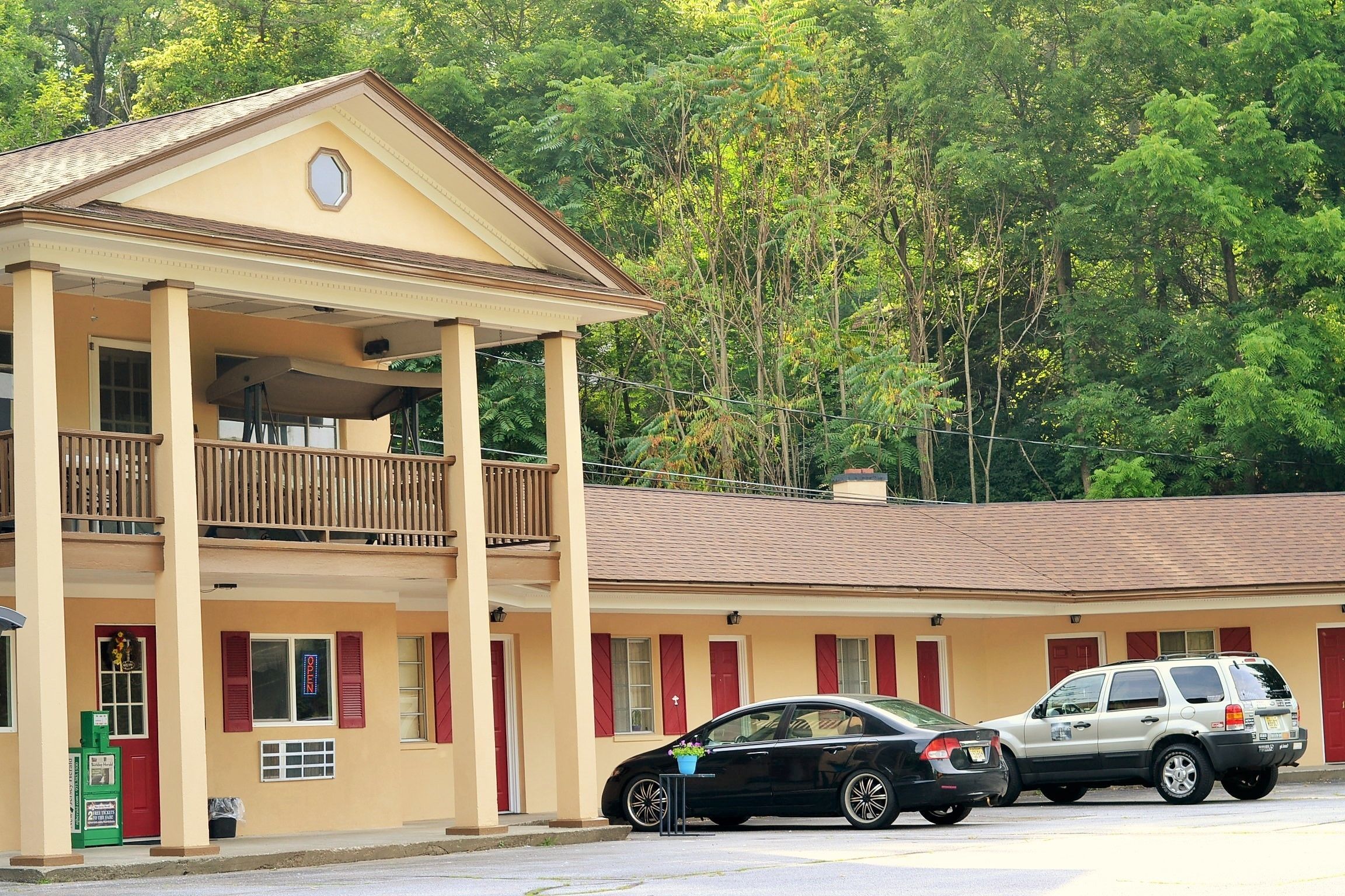 A two-story motel with a balcony on the upper floor, a covered front porch, and a parking area with two cars.