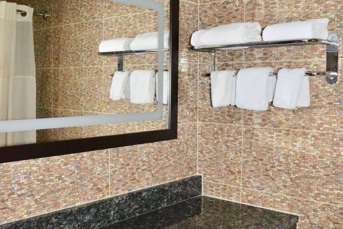 Un baño con encimera de granito, un lavamanos blanco, un espejo, un perchero para toallas y un inodoro.