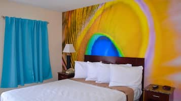 Habitación de hotel con cama, mesita de noche, lámpara y un cuadro abstracto colorido en la pared.