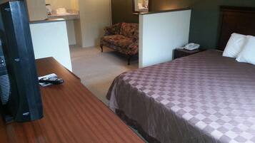 A hotel room with a bed, a desk with a television, a chair, and a nightstand with a phone.