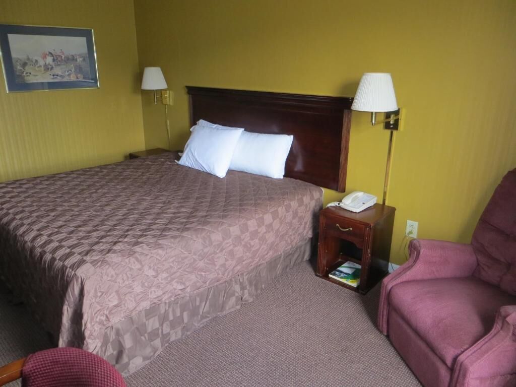 A hotel room with a large bed, two bedside lamps, a nightstand with a phone, a chair, and a painting on the wall.