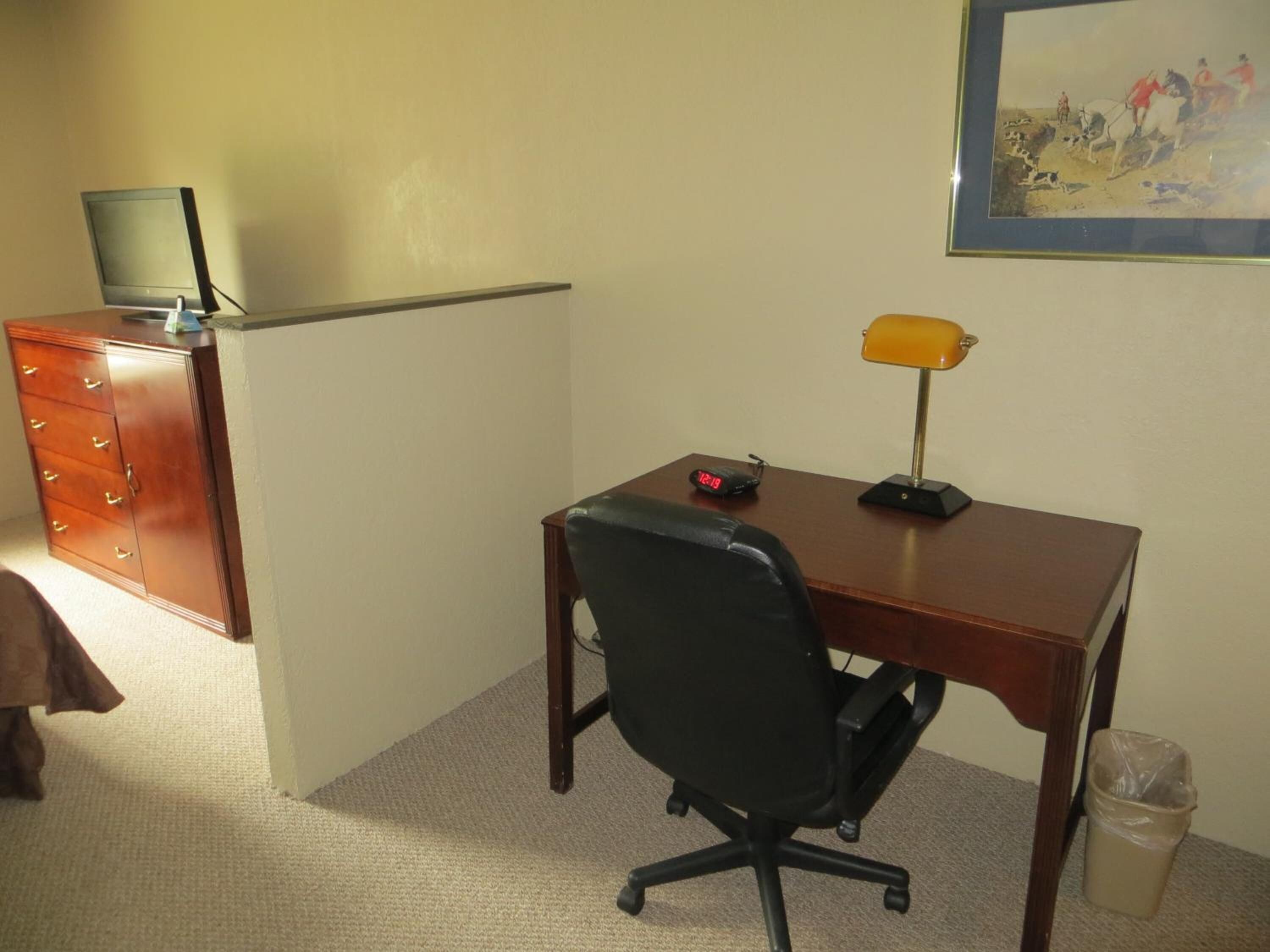 A small office space with a desk, chair, computer, lamp, and a trash can.