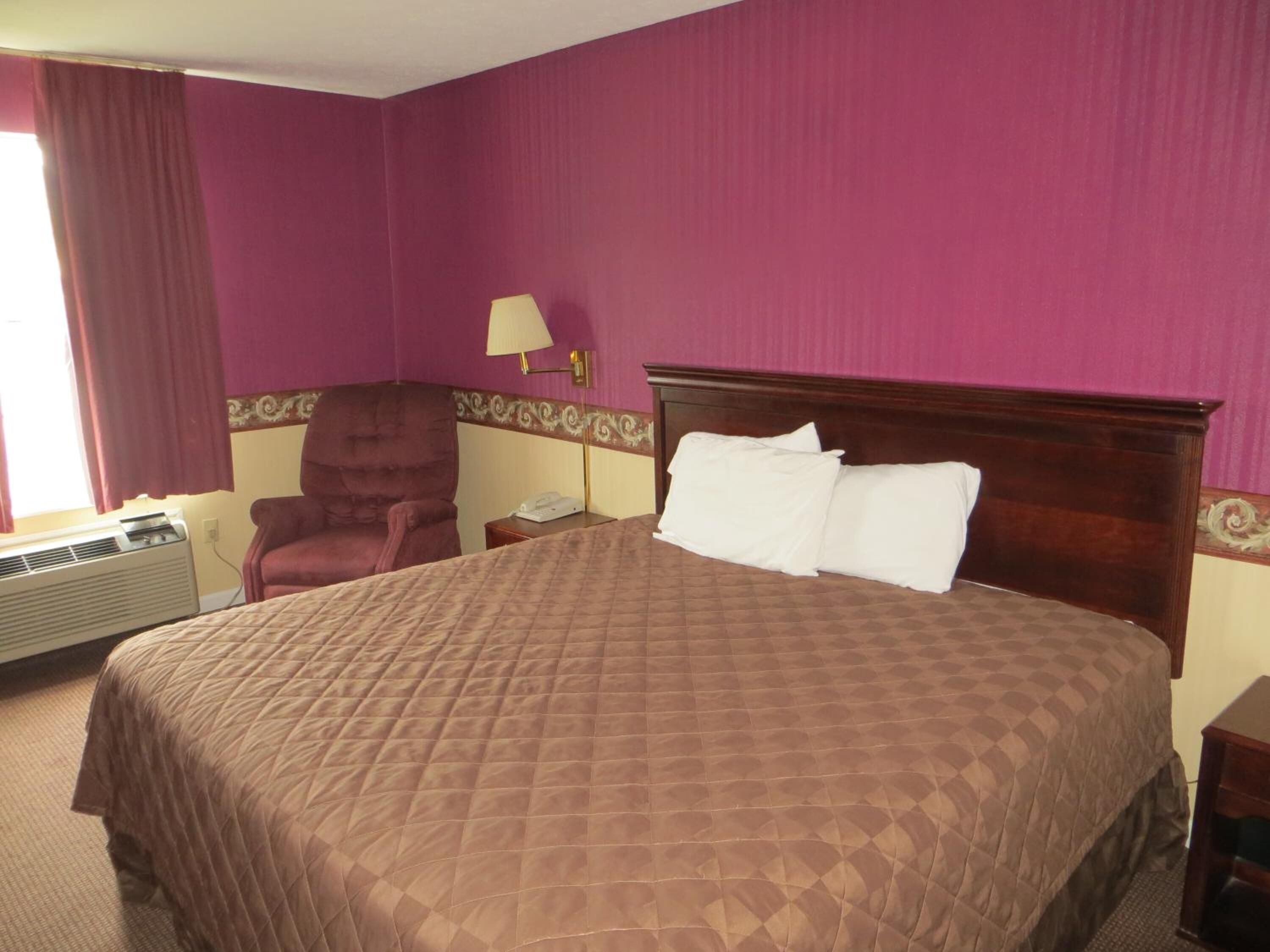 A hotel room with a large bed, a chair, a nightstand, and a lamp.
