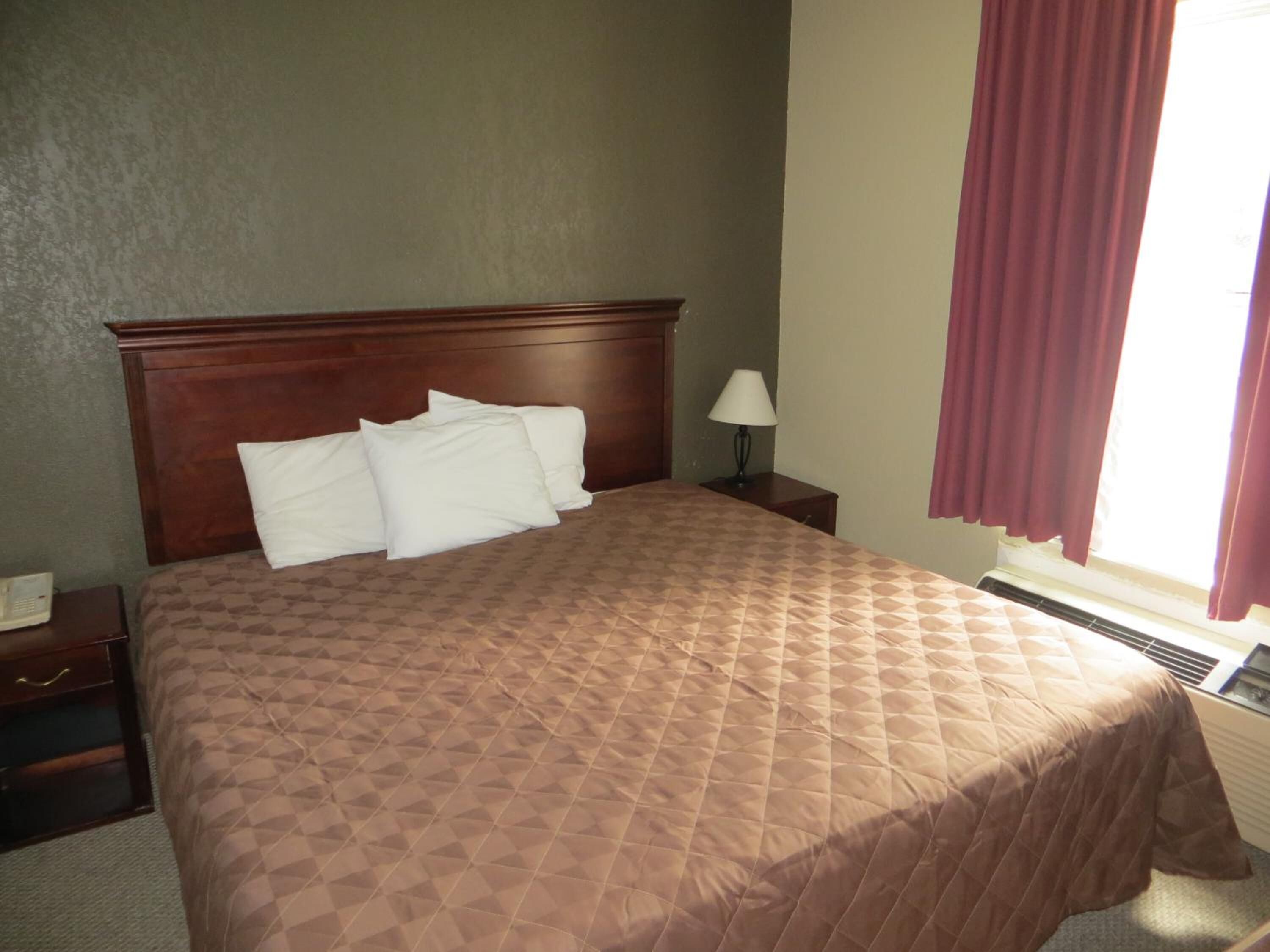 A neatly made bed with a brown quilt, a wooden headboard, a bedside lamp, and a nightstand with a phone.