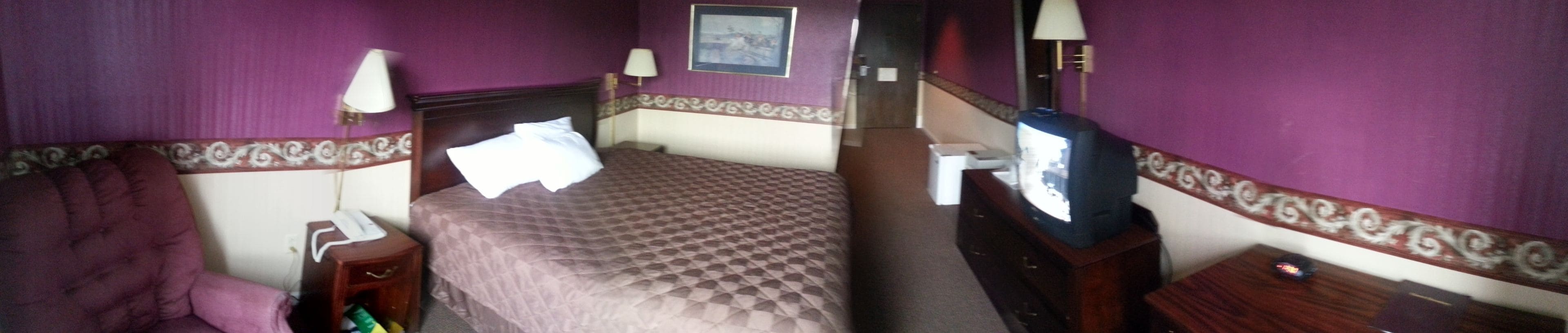 Una habitación de hotel con cama, una silla, un escritorio con teléfono y una televisión.