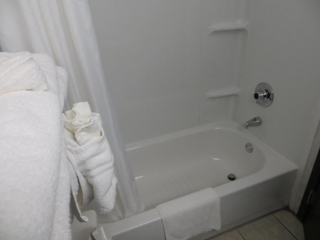 A white bathtub with a shower curtain, a towel, and a small sink.
