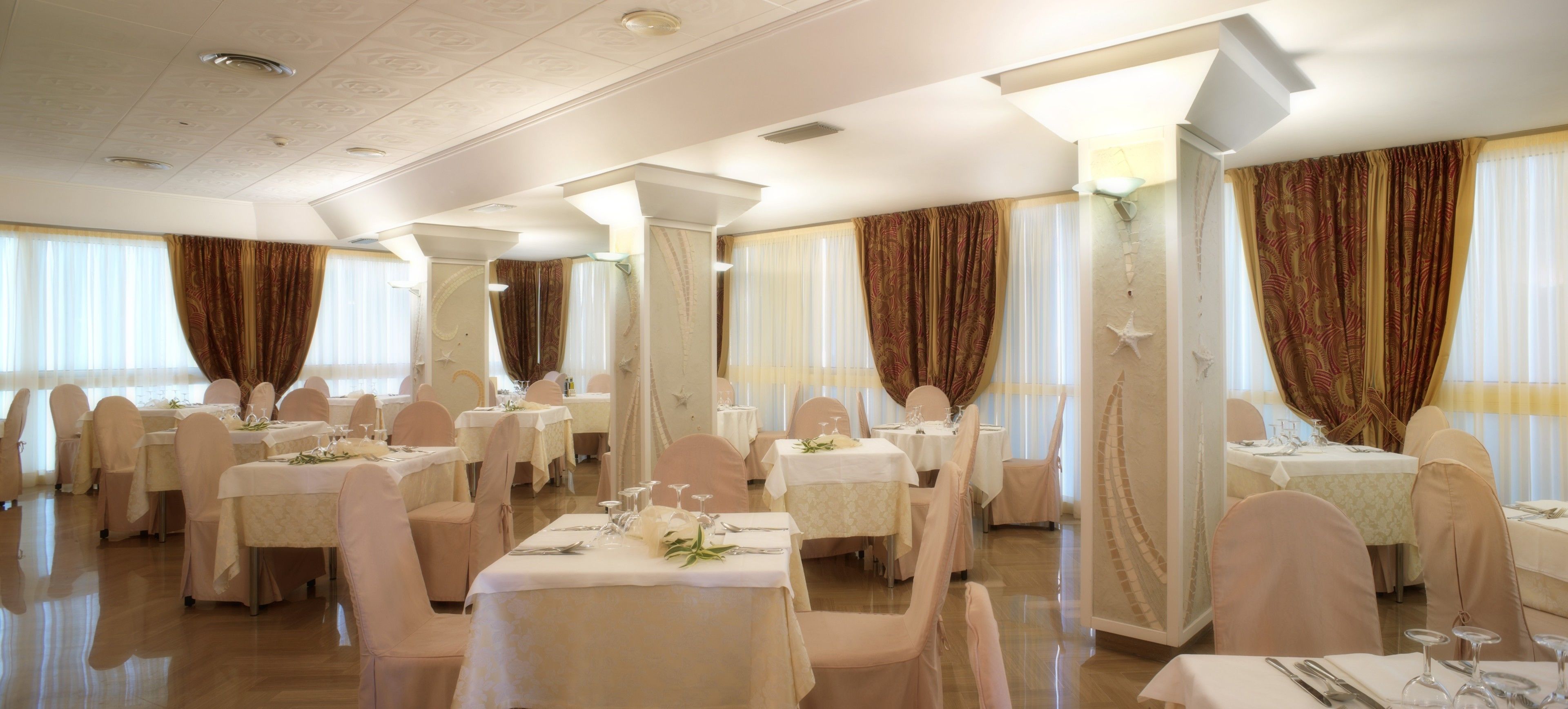 A banquet hall with multiple round tables, each set with white tablecloths and pink chairs.