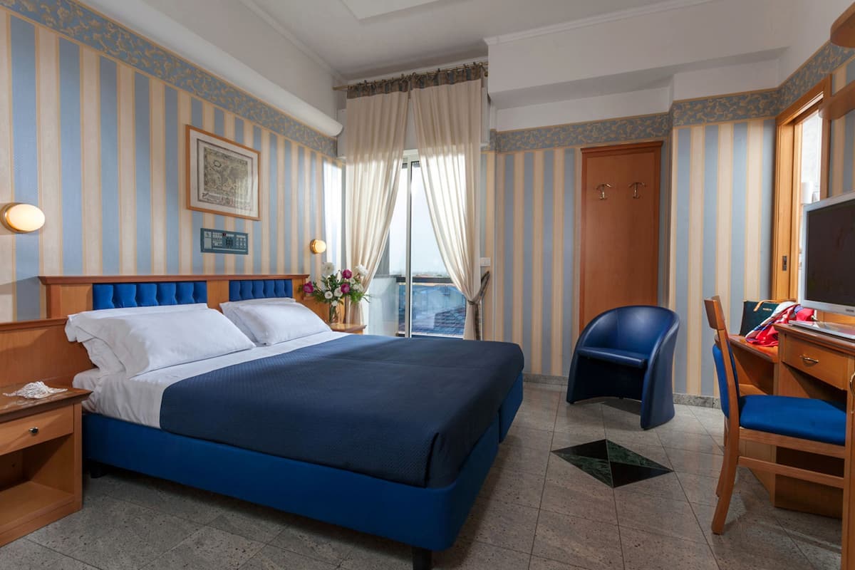 A hotel room with a large bed, a desk with a chair, a TV, and a window with curtains.