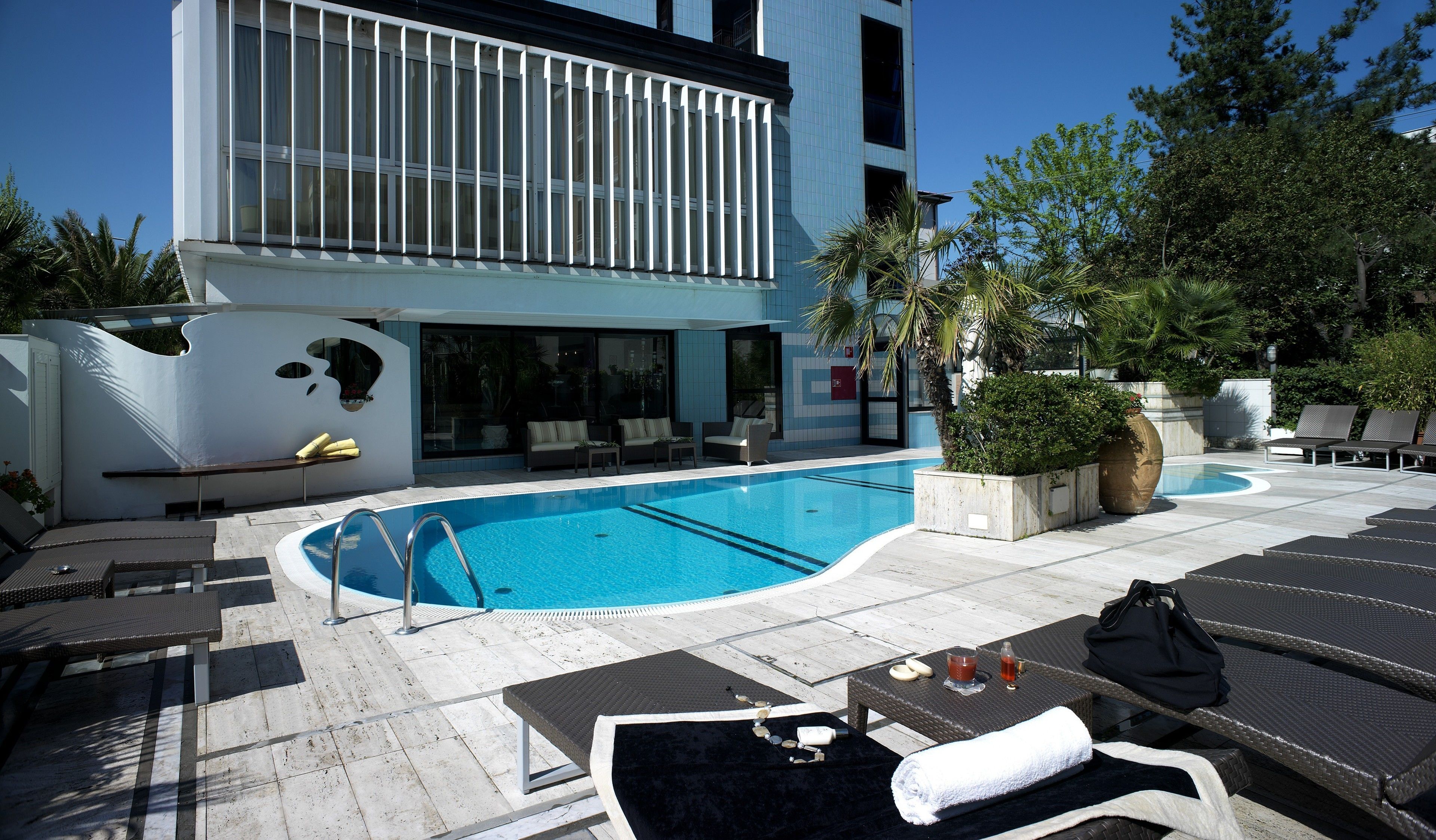A modern hotel pool area with a clear blue pool, lounge chairs, and a seating area with cushions.