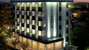 Un hotel moderno con varios balcones, una piscina y una fachada bien iluminada.