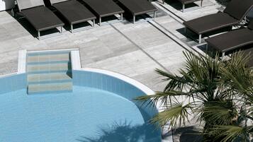 Una piscina con lettini da relax e una palma.